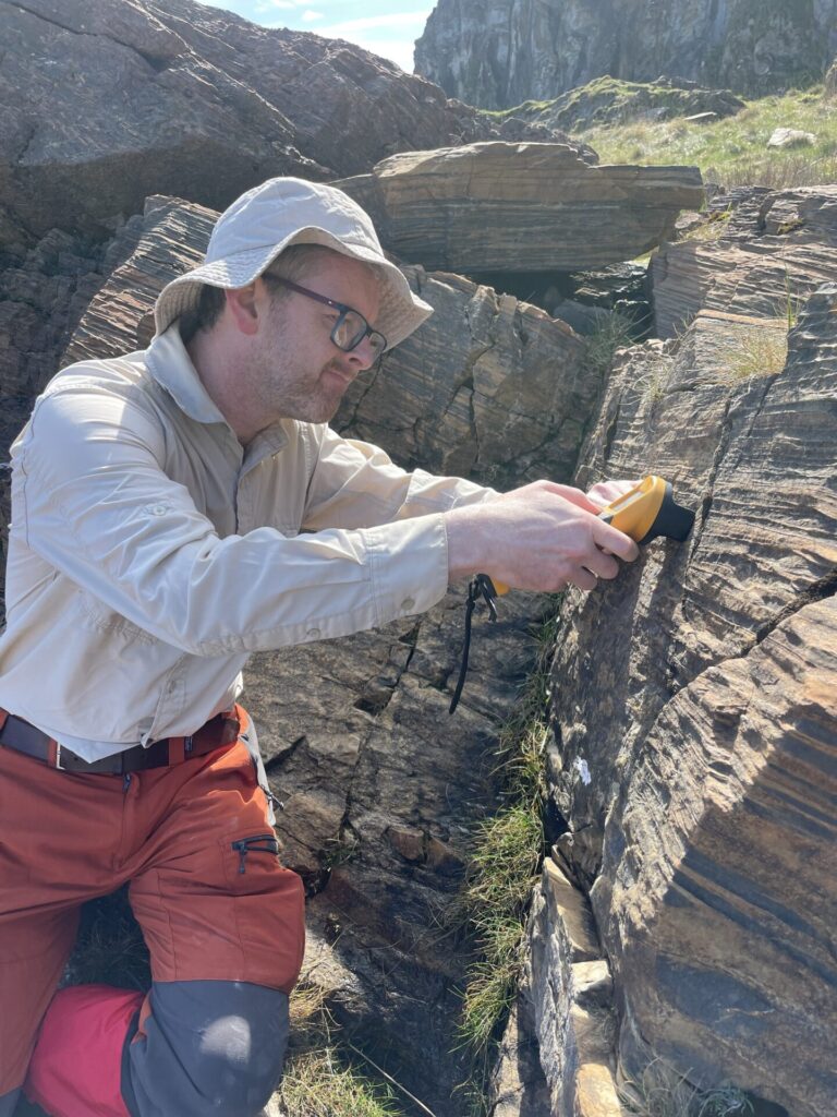 Above: Tom Gernon doing fieldwork on the Garvellach Islands, Scotland. Here he is using a magnetic susceptibility meter to record the magnetic signature of the rock layers through the sequence, which can reveal climatic oscillations. Photo courtesy of Elias Rugen.